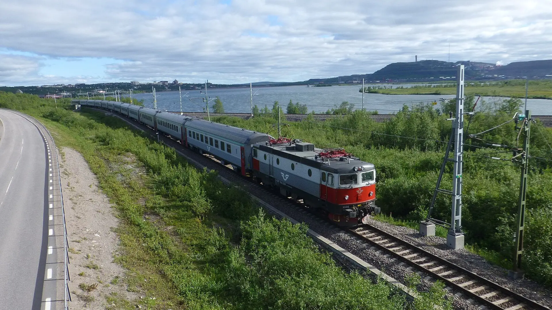 De nachttrein op de Malmbanan bij Kiruna in de zomer, met het meer Luossajärvi en de stad op de achtergrond
